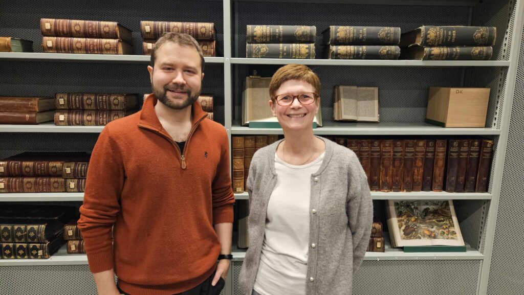 Bildet viser Helge Øvreness fra NFE og Mona Bjelland fra Kreftforeningen foran en bokhylle på Deichman bibliotek i Oslo.